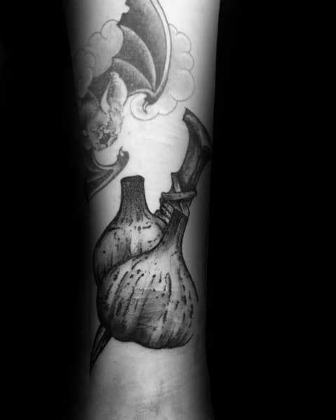 Black and grey garlic tattoo with a dagger piercing through it, featuring fine shading and bold details for a dark, gothic-inspired design.