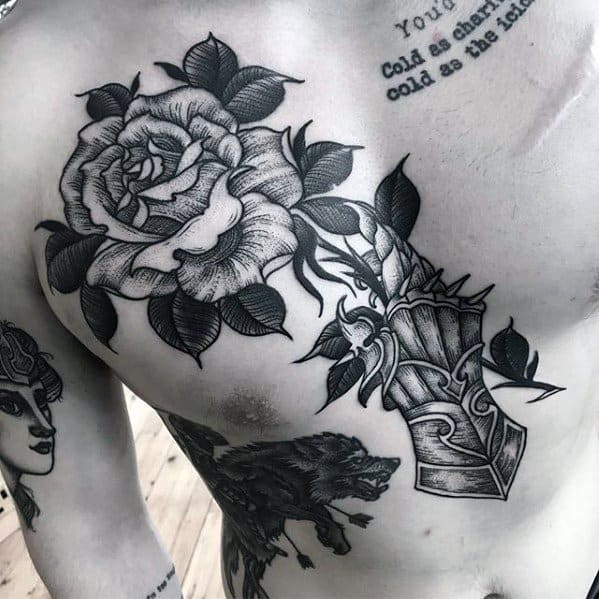 Blackwork tattoo of an armored gauntlet on the chest holding a large blooming rose, with detailed leaves and bold shading throughout.