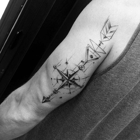 Geometric arrow and compass tattoo with celestial symbols, bold lines, and abstract triangular elements on the upper arm.