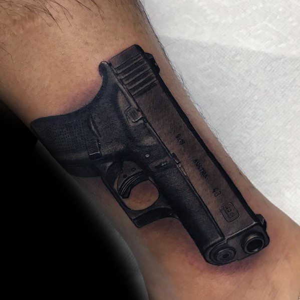 Realistic black and grey tattoo of a Glock pistol on the ankle, featuring detailed shading and depth to create a striking three-dimensional effect.