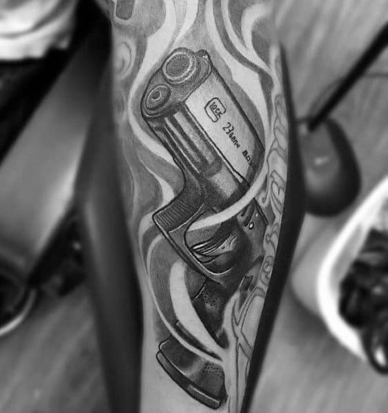 Realistic black and grey tattoo of a Glock pistol on the leg, featuring smoke-like patterns around it for a dynamic and bold visual effect.