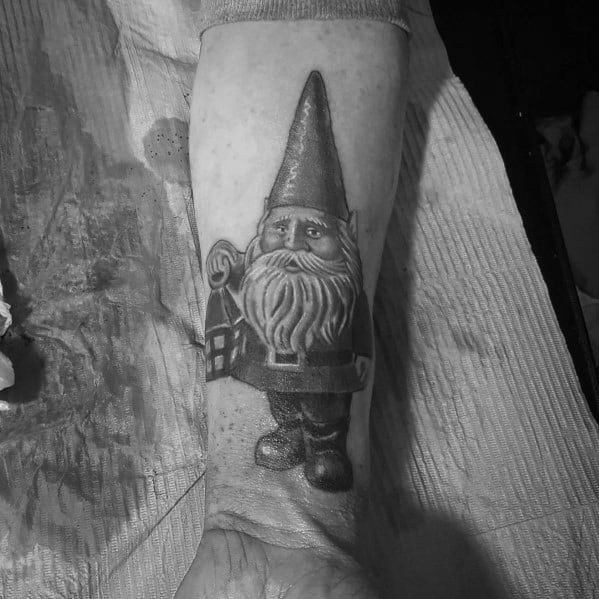 Black and white tattoo of a gnome with a tall hat and long beard, holding a lantern, standing in a classic pose with detailed shading.
