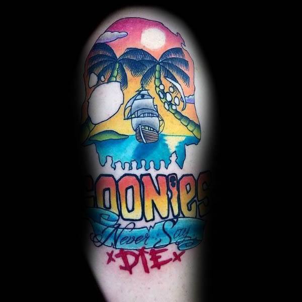 Colorful tattoo of The Goonies featuring a tropical island scene shaped like a skull, with a pirate ship and the phrase "Goonies Never Say Die".