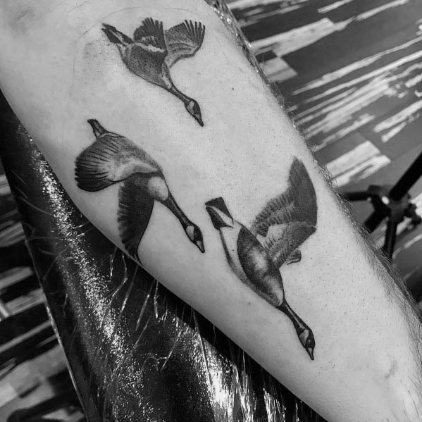 Black and gray tattoo of three geese in flight, inked on the forearm with fine shading and realistic details to capture movement and depth.