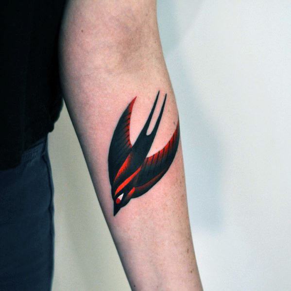 Stylized swallow tattoo on the forearm with bold black and red gradient wings and clean, sharp lines for a dynamic look.