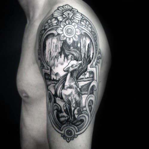 A stunning black and grey tattoo featuring a greyhound in an elegant pose, framed by ornate floral designs and intricate background details that evoke a vintage or mythical atmosphere.