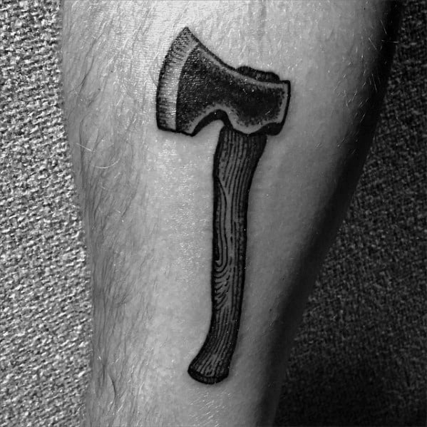 Black and grey hatchet tattoo on the leg with bold shading, a wood-grain textured handle, and a rugged blade for a classic and strong design.