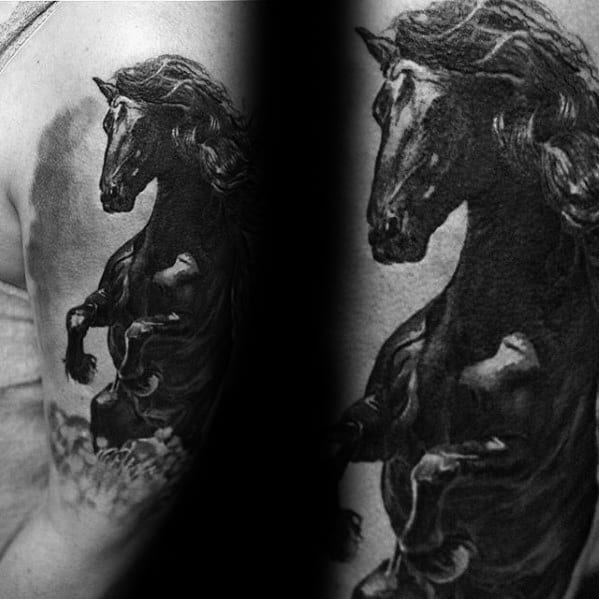 Realistic black and grey tattoo of a powerful rearing horse with flowing mane and detailed muscle shading on the upper arm