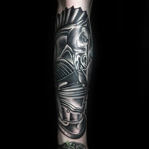 Black and grey tattoo of a horse head emerging from a knight's helmet, blending realism with armor detailing on the forearm