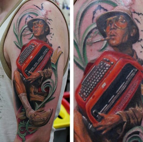 Realistic Hunter S. Thompson tattoo featuring him in aviator glasses and a bucket hat, holding a red typewriter with a cigarette in his mouth.