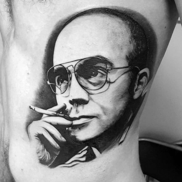 Black and white Hunter S. Thompson tattoo featuring a highly detailed portrait with aviator glasses, a cigarette, and bold shading for a realistic effect.