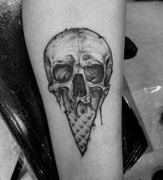 Black and grey tattoo of a detailed skull merging into an ice cream cone, featuring fine shading and realistic textures for a bold, gothic design.