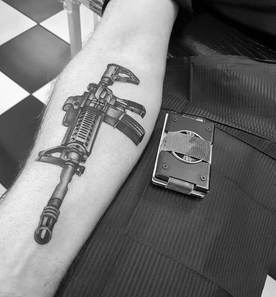Black and grey AR-15 tattoo on the forearm, featuring a realistic design with a tactical grip and magazine, symbolizing strength and resilience.