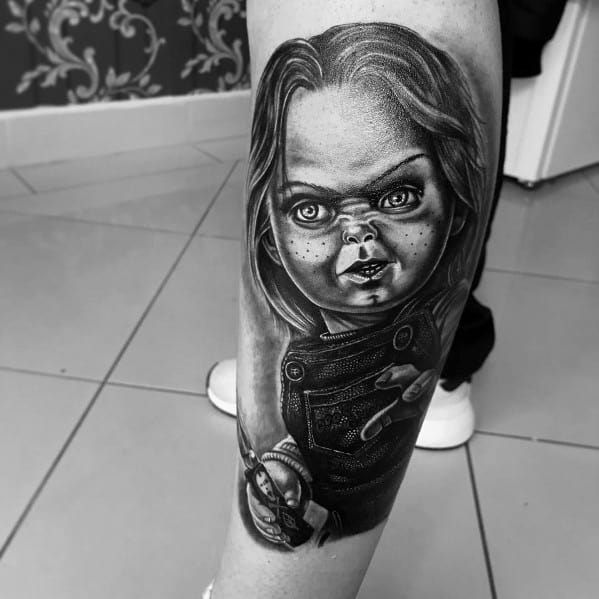 Black and grey Chucky tattoo with realistic shading, featuring his eerie stare, stitched details, and a jack-in-the-box clown for a chilling horror design.