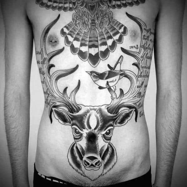 Black and grey elk tattoo on the stomach, featuring bold antlers, intricate shading, and symbolic elements like a bird and text for a striking design.