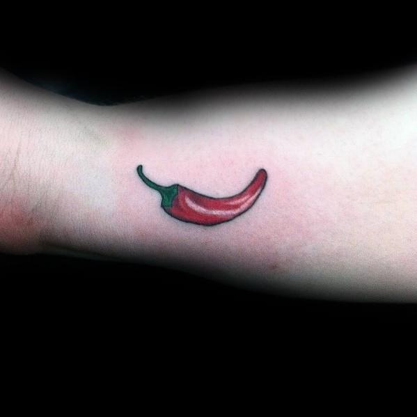 Small red chili pepper tattoo on the wrist with a green stem and subtle shading for a simple yet bold design.
