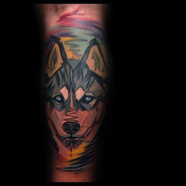 Geometric Siberian Husky tattoo on a man's leg, featuring bold angular shapes, vibrant colors, and piercing blue eyes for a striking modern design.