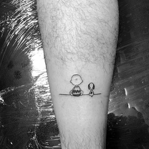 Minimalist black and white tattoo of Charlie Brown and Snoopy sitting side by side on a thin line, placed on a person's leg.