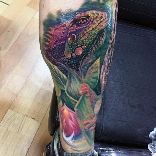 Vibrant iguana tattoo on leg with rich purple and green tones, surrounded by lush leaves and a blooming pink flower