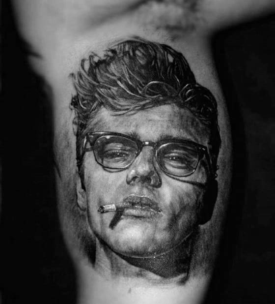 Realistic black and grey tattoo of James Dean with tousled hair, thick glasses, and a cigarette hanging from his lips.