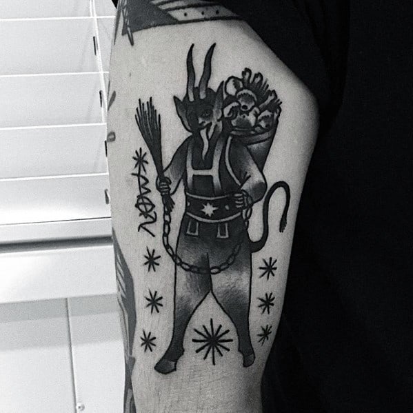 Blackwork Krampus tattoo on upper arm showing the horned figure holding birch branches, with a child in a basket and star accents around.
