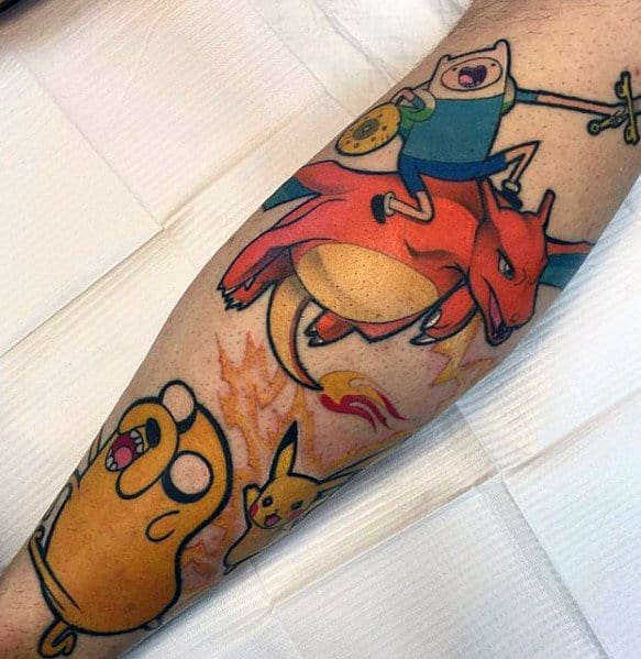 Colorful mashup tattoo of Finn riding Charizard with Jake and Pikachu beside him, blending Adventure Time and Pokémon themes on the leg.