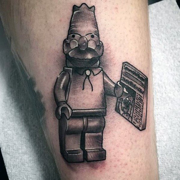 Black and grey tattoo of Lego Grandpa Simpson holding a newspaper, featuring detailed shading and cartoon-accurate facial features.