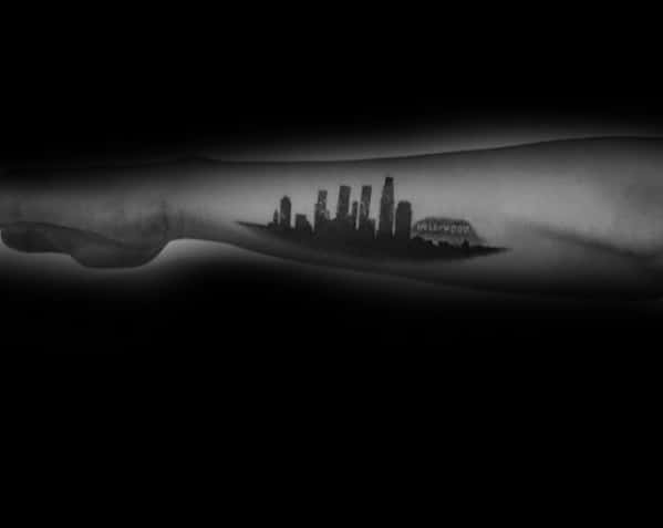 Minimalist forearm tattoo of Los Angeles skyline with Hollywood sign in black ink on inner arm.