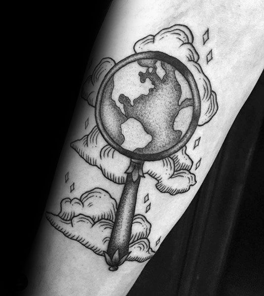 Tattoo of a magnifying glass focusing on the world, surrounded by clouds and sparkles, creating a bold, illustrative design with a sense of exploration.