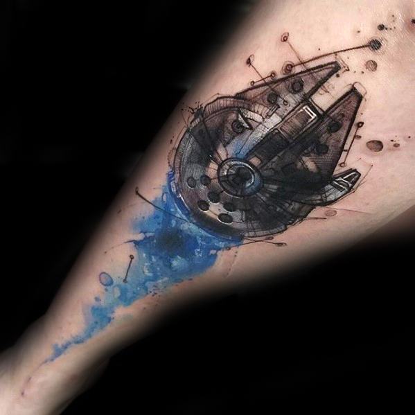 Watercolor-style Millennium Falcon tattoo with abstract blue and black ink splashes and sketch-like detailing on the forearm.