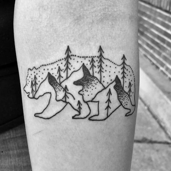 Minimalist bear-shaped mountain tattoo on the forearm, featuring trees, peaks, and dot work for a nature-inspired wilderness design.