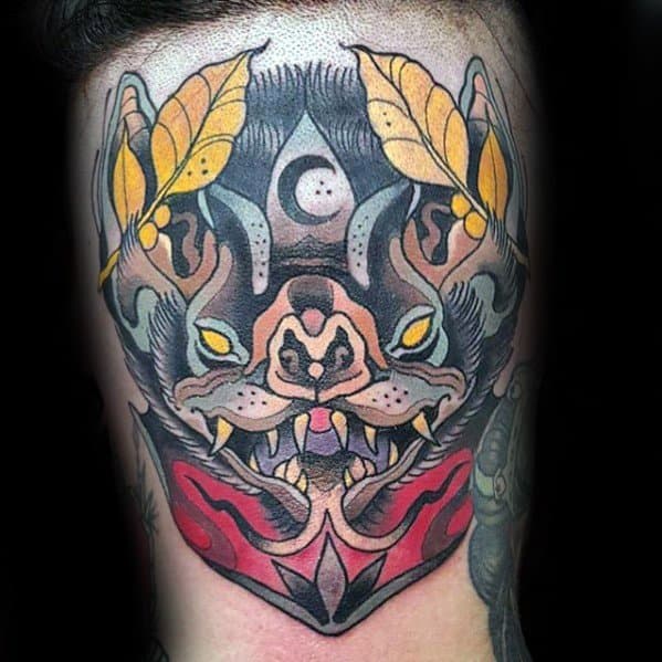 Neo-traditional bat tattoo with a fierce face, yellow leaves, crescent moon, and symmetrical red and black design elements.