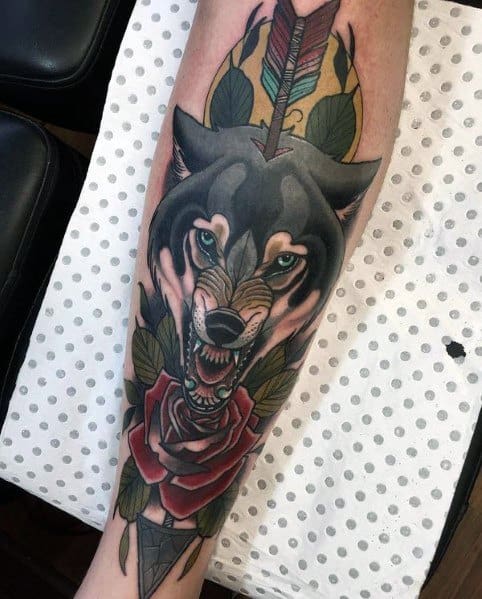 Neo-traditional tattoo of a snarling wolf with piercing green eyes, an arrow through its head, a bold red rose, and intricate shading.