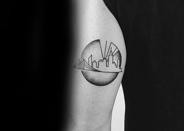 Minimalist black line tattoo of the New York City skyline with a bridge and circular shading detail on the upper arm.