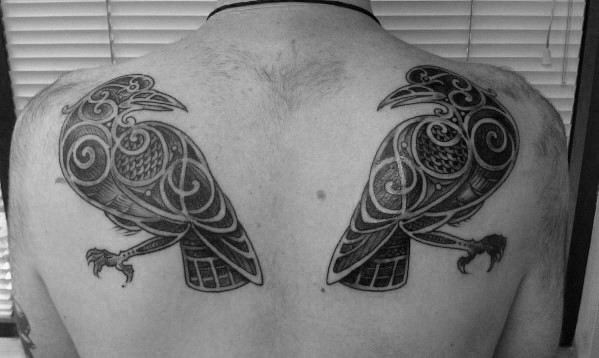Symmetrical back tattoo of Huginn and Muninn in a Celtic-inspired design, facing inward with intricate black linework and spirals.