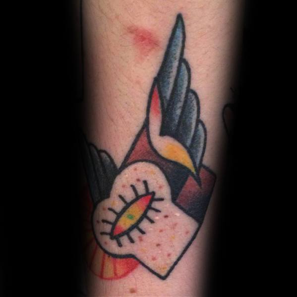Colorful tattoo of a slice of bread with an eye in the center and wings, featuring a bold traditional style with vibrant shading and dynamic details.