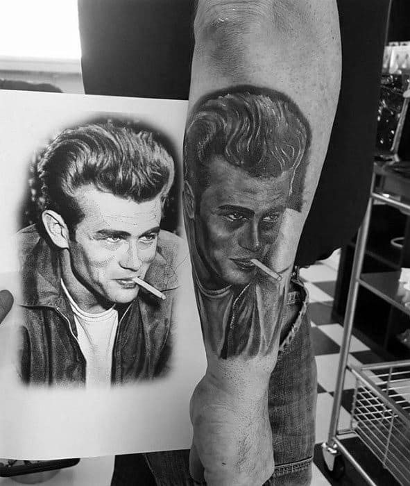 Forearm tattoo of James Dean based on a classic photo, showing him in a jacket with a cigarette, recreated in detailed black and grey realism.