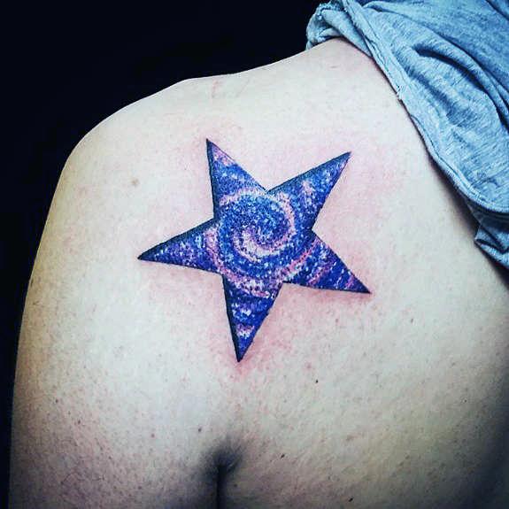 Colorful galaxy-themed star tattoo on shoulder, featuring a swirling cosmic design in shades of purple, pink, and blue.