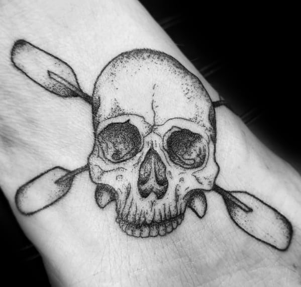 Black and grey tattoo of a skull with crossed paddles, blending nautical and pirate themes, symbolizing adventure, resilience, and the wild spirit.