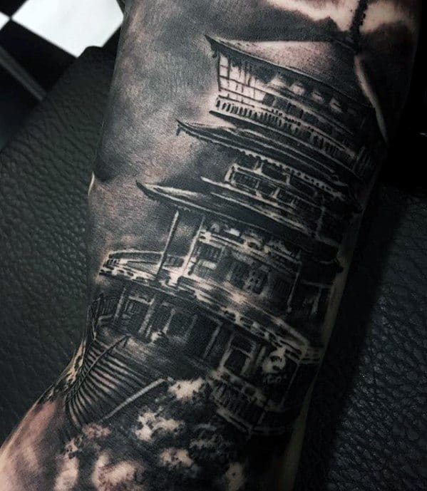 High-contrast black and grey tattoo of a Japanese pagoda with dramatic lighting, bold shadows, and cloudy sky detailing.