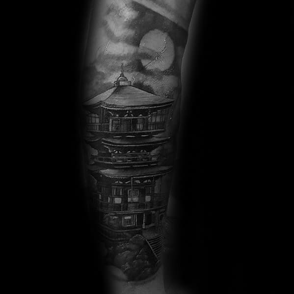 Dark forearm tattoo of a Japanese pagoda with a glowing moon and cloudy night sky, featuring deep shadows and fine details.