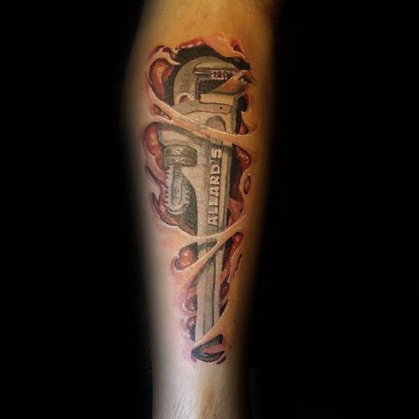Realistic tattoo of a pipe wrench beneath torn skin, revealing the name “Allard’s” with vivid shading and 3D muscle detailing.