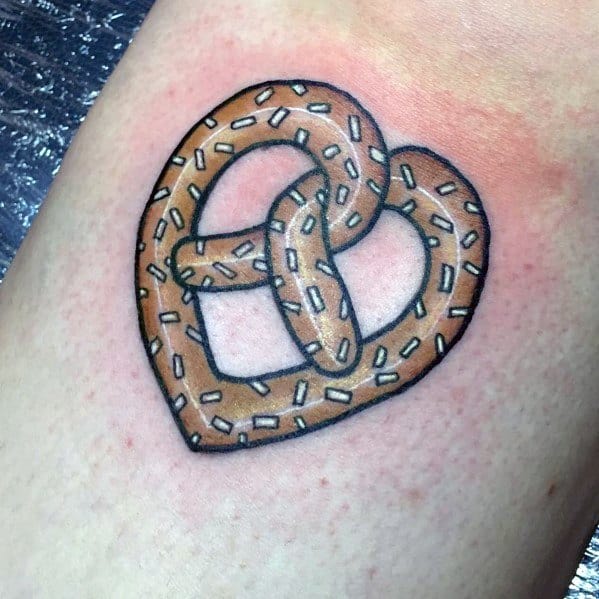 Heart-shaped pretzel tattoo with a golden brown hue, bold black outline, and white salt details for a crisp and clean design.