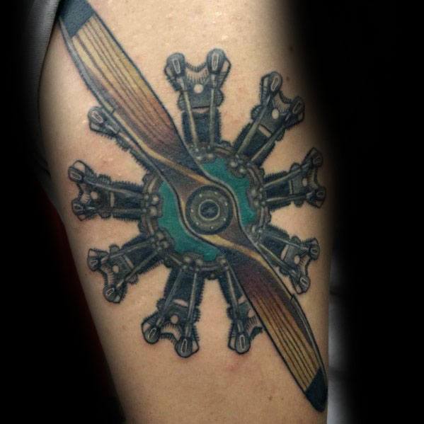Detailed upper arm tattoo of a radial aircraft engine with a wooden propeller, featuring bold outlines, shading, and a touch of color for contrast.