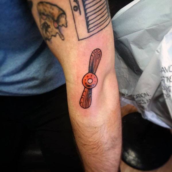 Small forearm tattoo of a wooden propeller with bold black outlines and subtle orange shading, creating a classic aviation-inspired design.