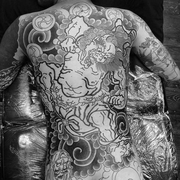 Black and grey Raijin full back tattoo in progress, featuring bold thunder god, swirling clouds, and detailed traditional linework.