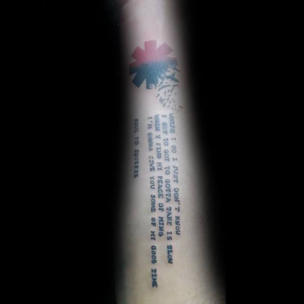 Forearm tattoo featuring Red Hot Chili Peppers lyrics in a clean, typewriter-style font, with the band's logo fading into an abstract design.