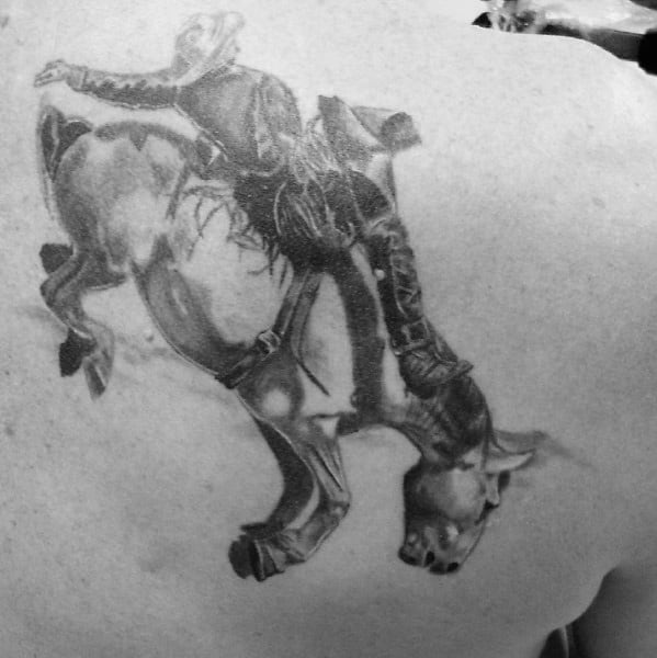 Realistic black and grey tattoo of a cowboy riding a bucking bull, featuring detailed shading, intense motion, and a rugged Western rodeo theme.