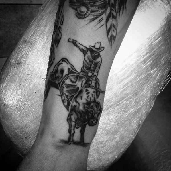 Black and grey tattoo of a cowboy riding a bucking bull, featuring fine shading, bold details, and a Western rodeo theme on the forearm.