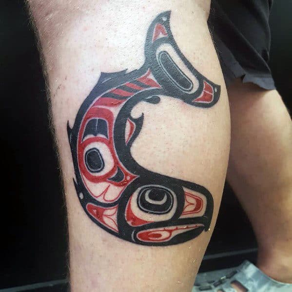Tribal-style salmon tattoo in bold black and red, inspired by Indigenous art, featuring intricate patterns for a striking and symbolic leg design.